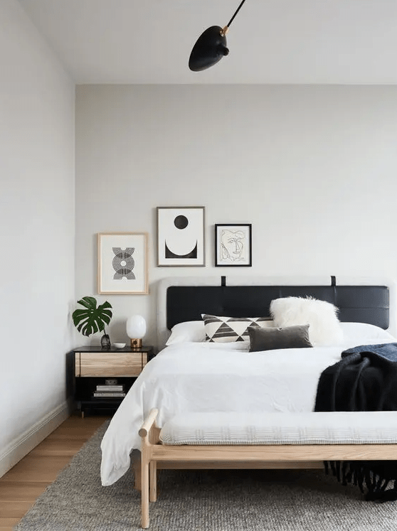 a modern boho bedroom with a bed with a black headboard, a bench, a nightstand and a small gallery wall