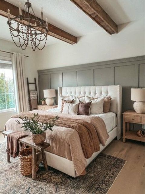 a modern farmhouse bedroom with grey paneling, a bed with cozy bedding, a stained bench, a beaded chandelier and wooden beads