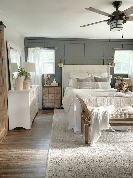 a modern neutral bedroom with a grey paneled wall, a creamy upholstered bed with neutral bedding, stained nightstands and a white dresser