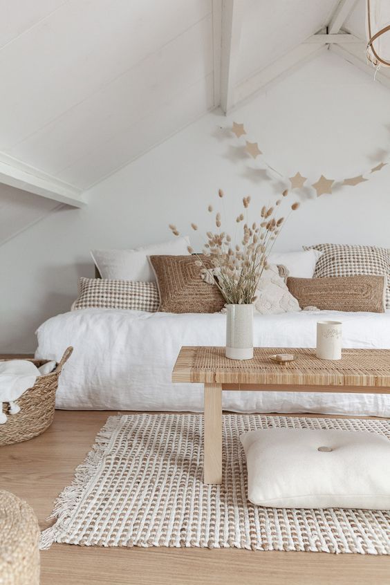 a neutral boho bedroom with a bed, lots of pillows, a woven bench, some neutral decor and textural linens and pillows