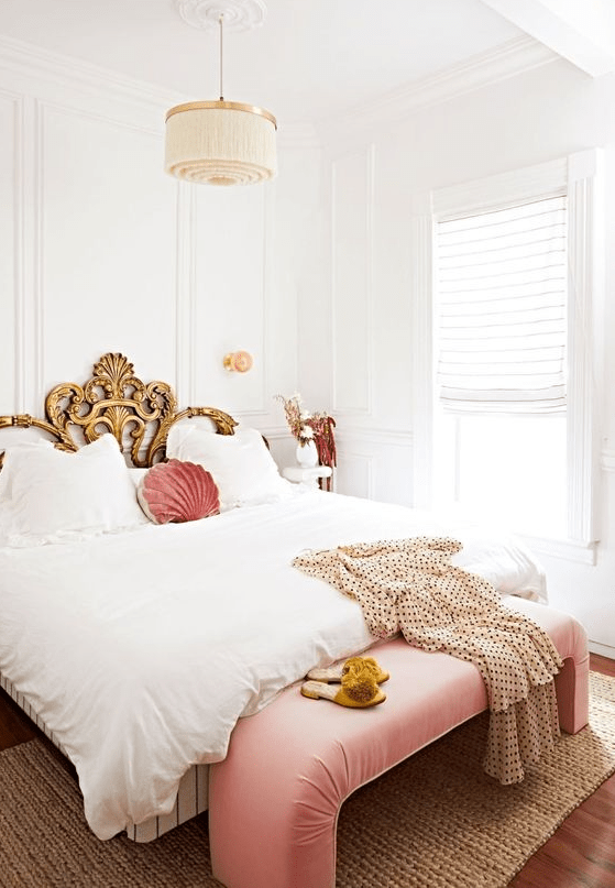a refined bedroom in neutrals, with a gold exquisite bed, a pink bench and pillow plus a tassel chandelier