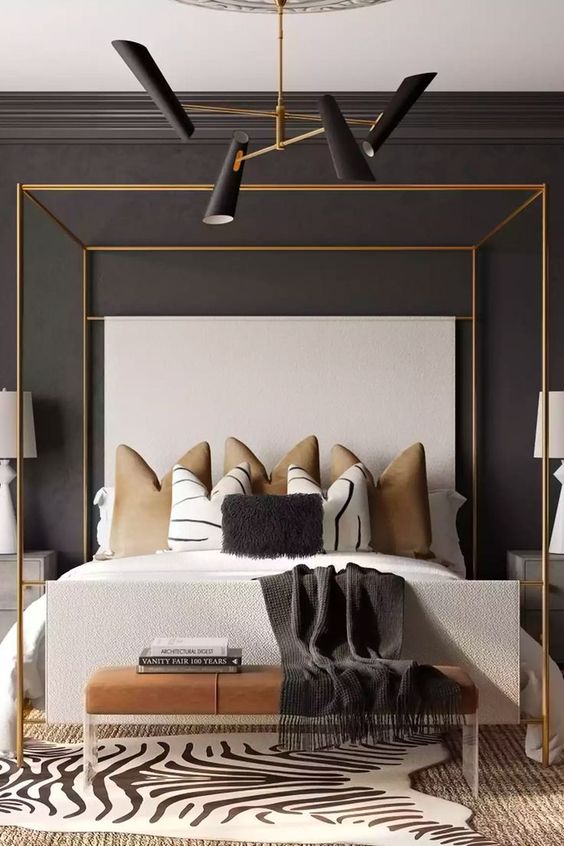 a refined moody bedroom with a black accent wall, a gold frame bed and chic pillows, a leather bench and layered rugs