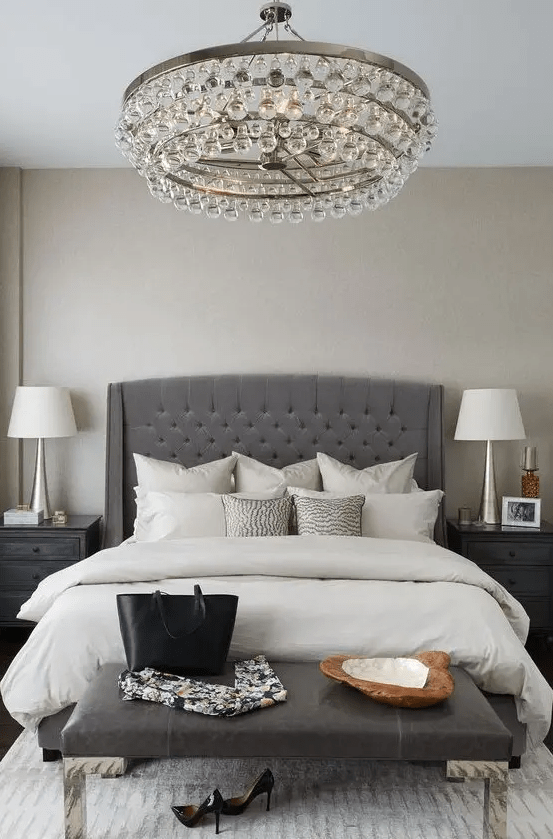 an elegant charcoal grey tufted wingback headboard, a crystal chandelier and a leather bench make up a glam modern space