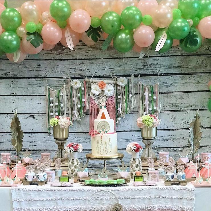 a colorful pink and green dessert table with dream catchers, feathers, blooms and lots of balloons