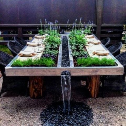 an outdoor dining table with planters with fresh greenery and herbs for eating and a waterfall will be a statement in your garden
