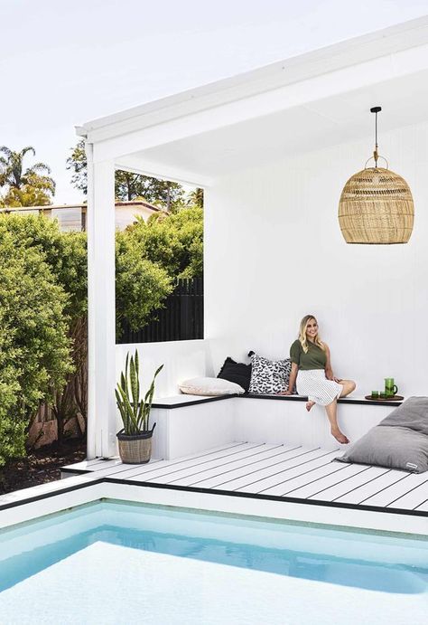 a white deck with a built-in bench with storage, printed pillows, a wicker lamp and potted plants
