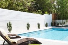 11 stylish curved wooden loungers with pillows and planted cacti along the pool for a cool minimal look