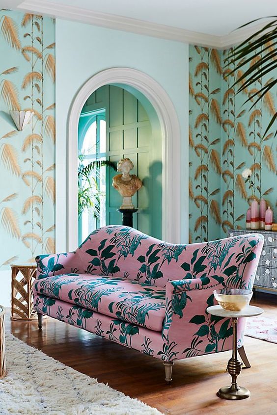 a pink botanical print sofa with a curvy back finishes off the space with green leaf print wallpaper