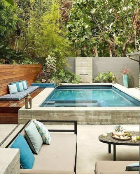 a cushion and pillows right on the deck, potted plants and lanterns, some comfortable furniture by the pool side