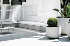 26 a minimalist white pool cabana with black pendant lamps, simple wooden benches with upholstery, potted plants and a coffee table