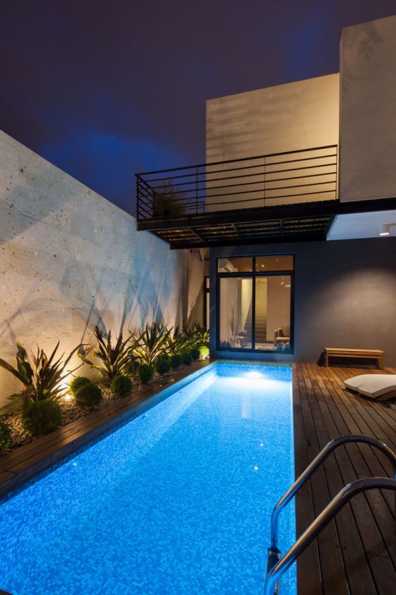 a bold outdoor tropical space with a long and narro wpool with lights, a wooden deck, growing plants and lights is cool