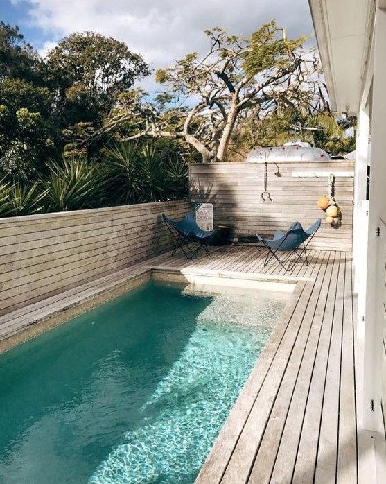 a chic contemporary backyard fully done with a wooden deck, butterfly chairs and a long and narrow pool