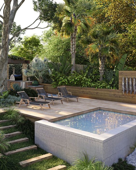 a contemporary outdoor space with a wooden deck, a small plunge pool raised above the ground and trees and greenery
