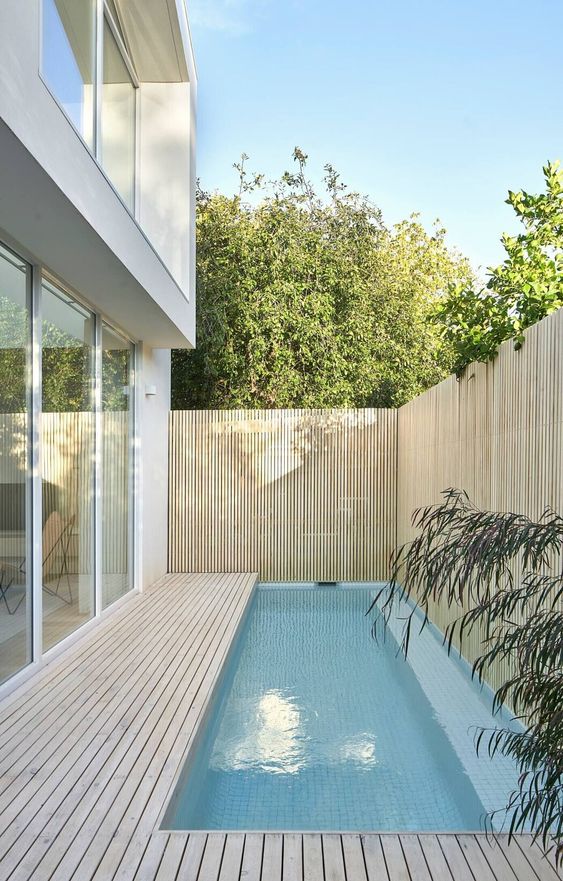 a contemporary outdoor space with a woodne deck and a small and narrow pool plus a wood slat fence around