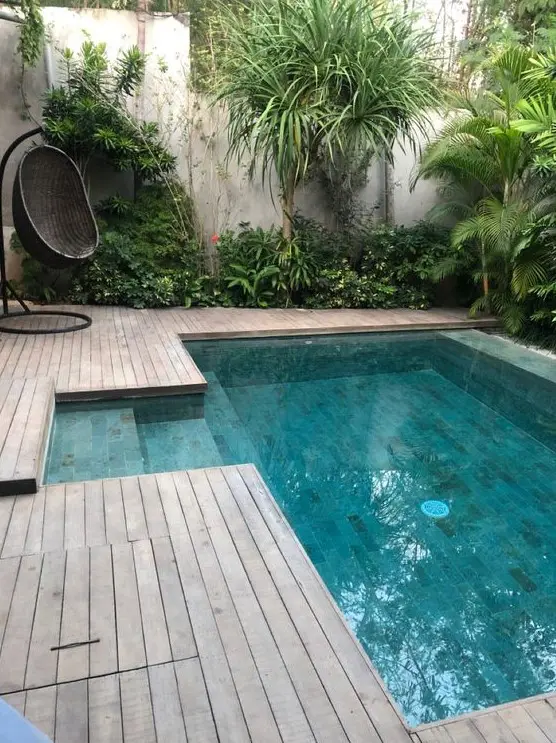 a cool tropical outdoor space with a wooden deck, trees and greenery around, a black woven egg shaped chair and a plunge pool is cool