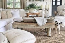 a cozy farmhouse living room with neutral upholstered furniture, a wooden coffee table and a stool on casters plus whitewashed candle holders