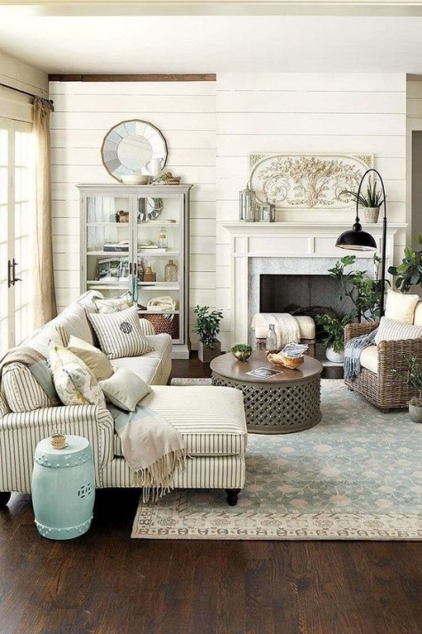 a cozy farmhouse space with a non-working fireplace, neutral upholstery, an aqua side table, a glass armoire
