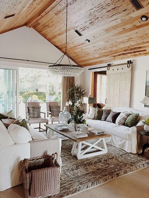 a farmhouse living room with much natural wood, a crystal chandelier, cozy and simple furniture and a barn door