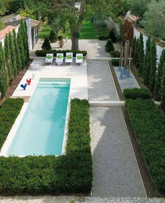a gravel covered backyard with perfect greenery and a small narrow pool, some loungers and decor is very chic
