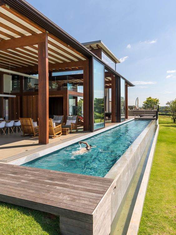 a large outdoor space with a deck, with a dining space and a seating zone, a long and narrow pool with a deck and some views