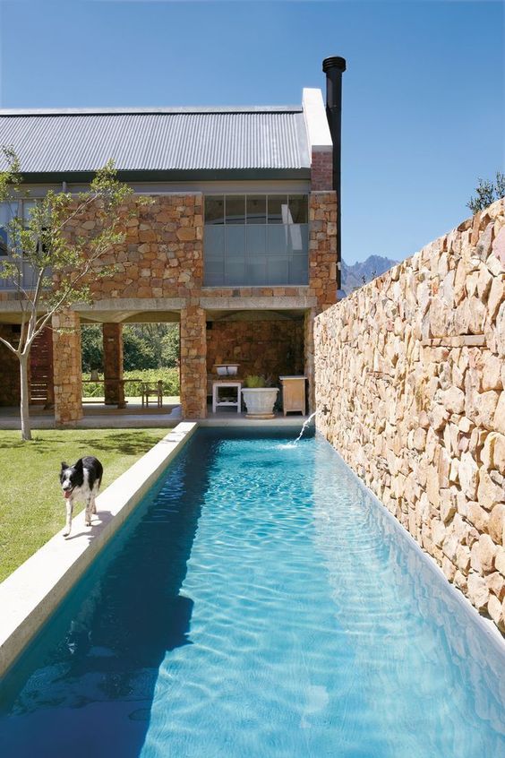 a long and narrow pool with a stone fence and a waterfall is a lovely space to chill in, it's great to have a rest