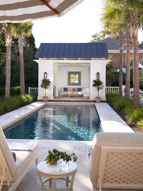 a lovely outdoor space with greenery, a pool with a stone deck, a cabana and some loungers under an umbrella is amazing