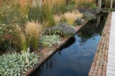 a lush and textured garden with bushes, grasses and leaves and a long and narrow pool clad with brick around that looks pretty natural