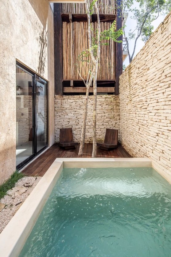 a minimal outdoor space with stone walls, a dark stained furniture, a plunge pool, some trees and wooden chairs