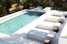 a minimalist backyard with a pool, antislip stone tiles that form a deck and steps, a series of loungers with stump side tables