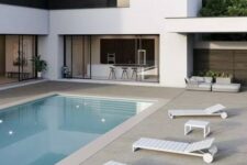 a minimalist outdoor space with a pool, a stone tile deck and white loungers, some neutral seating furniture is a very cool place