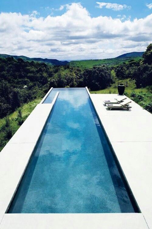 a minimalist outdoor space with a sleek deck, a long and narrow infinity pool plus a jaw-dropping view