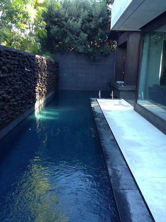 a minimalist outdoor space with a stone wall, a long and narrow pool, a tiled deck and nothing else to enjoy the fresh water