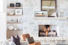 a modern farmhouse living space with a stone clad fireplace, a leather chair, built-in shelves, a white sofa