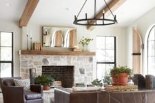 a modern laconic farmhouse living room with a stone fireplace, leather furniture, a vintage chandelier and potted greenery