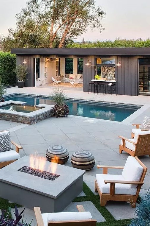 a modern outdoor space with a pool and a jacuzzi, a fire pit space and a pool house with a kitchen