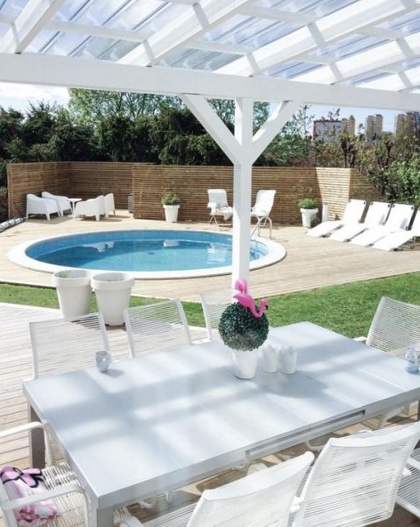 a neutral contemporary space with loungers and white garden furniture and a round pool clad in white, too