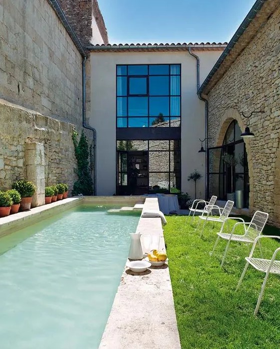 a small backyard with a lawn and a narrow pool done with stone, with potted greenery to make the space cozier