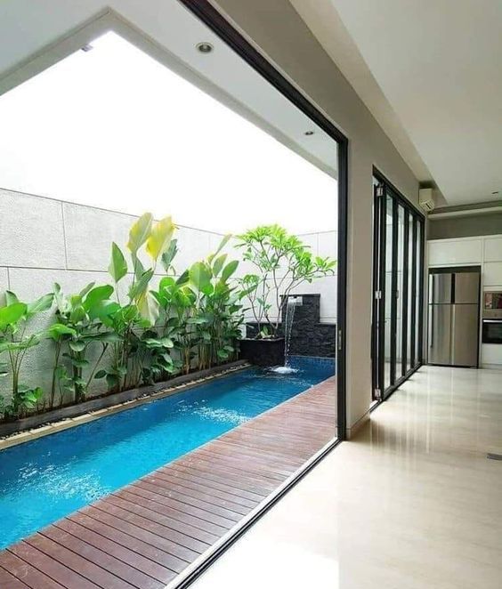 a small outdoor space with a wooden deck, a long and narrow pool, some potted plants and a waterfall is like a small heaven