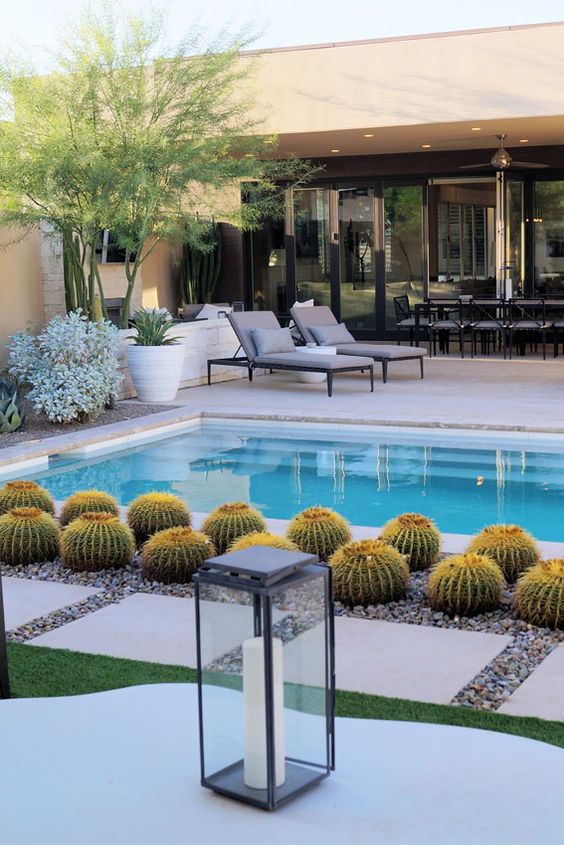 a super chic and elegant outdoor space with a stone deck, a pool, some cacti and tiles on gravel, with lanterns