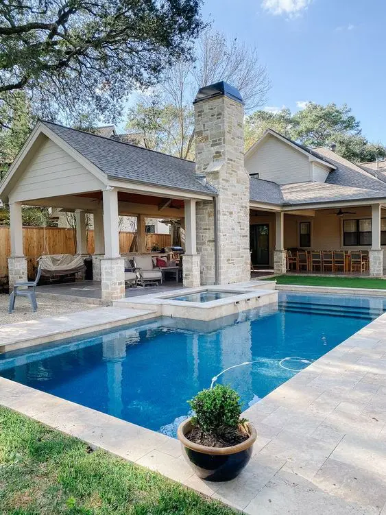 a traditional backyard with a stone deck, a pool with a tub, some potted greenery and a relax zone under the roof