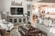 a vintage farmhouse living space with grey furniture, a stained ottoman with a leather top, a pendant lamp and printed pillows
