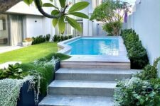 a welcoming outdoor space with a green lawn and some plants and trees, a pool with a wooden deck and steps and nothing else