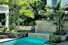 an elegant tropical backyard with a stone deck, a small pool and a tub, a couple of loungers, some greenery and trees