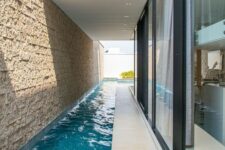 an indoor-outdoor long and narrow pool with a roof and some lights over it is a cool space to have a rest in