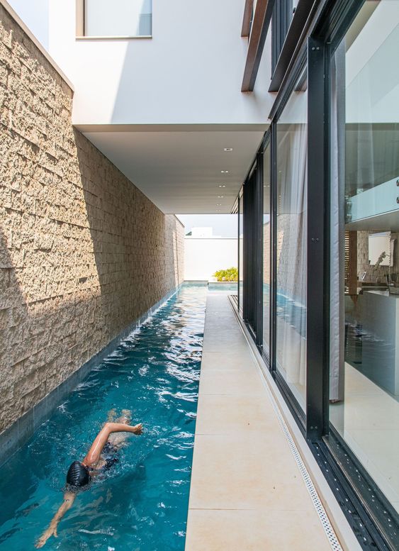 an indoor-outdoor long and narrow pool with a roof and some lights over it is a cool space to have a rest in