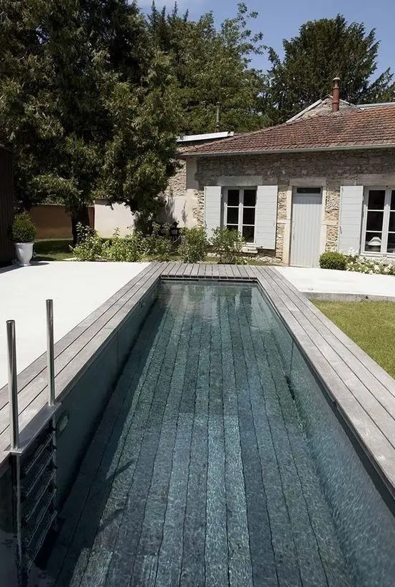 an outdoor space with a long and narrow pool and a wooden deck around is a lovely space to have a rest when it's hot