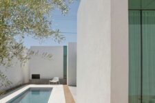an ultra-minimalist outdoor space with white walls and a tiled deck, a long and narrow pool and a single chair is super cool