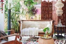 a Moroccan inspired porch with a colorful rug, beautiful wooden furniture and a carved screen, a leather ottoman and boho textiles