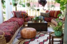 a boho Moroccan porch with a U shaped bench with boho upholstery, a bright rug, a leather ottoman and lots of potted plants