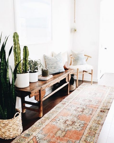 a boho chic entry with a boho rug, a dark stained wooden bench, potted cacti, printed pillows